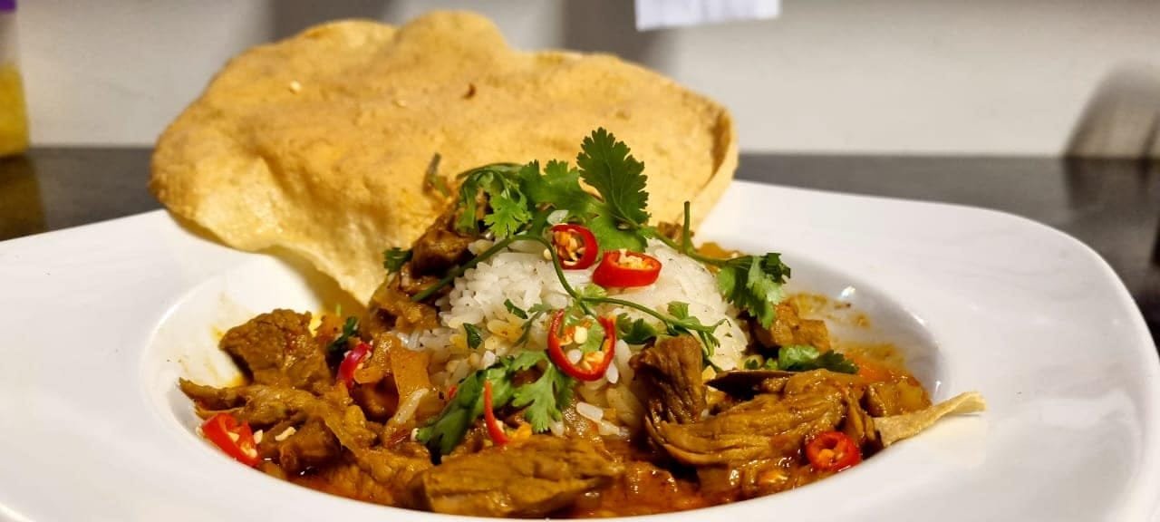 A curry served with rice, chilli, coriander and a poppadum