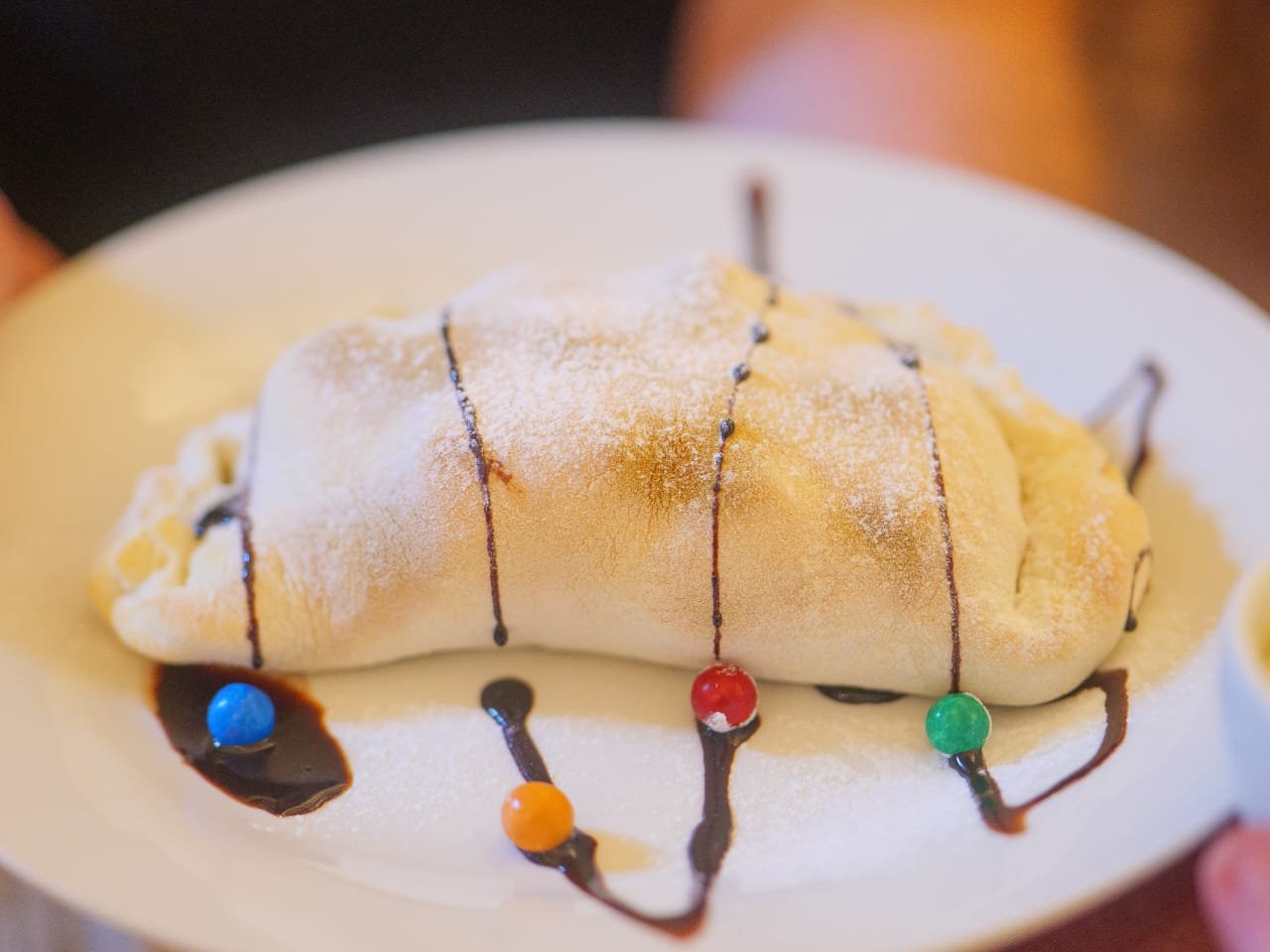 Sweet dessert calzone dusted with icing sugar and drizzled with chocolate sauce
