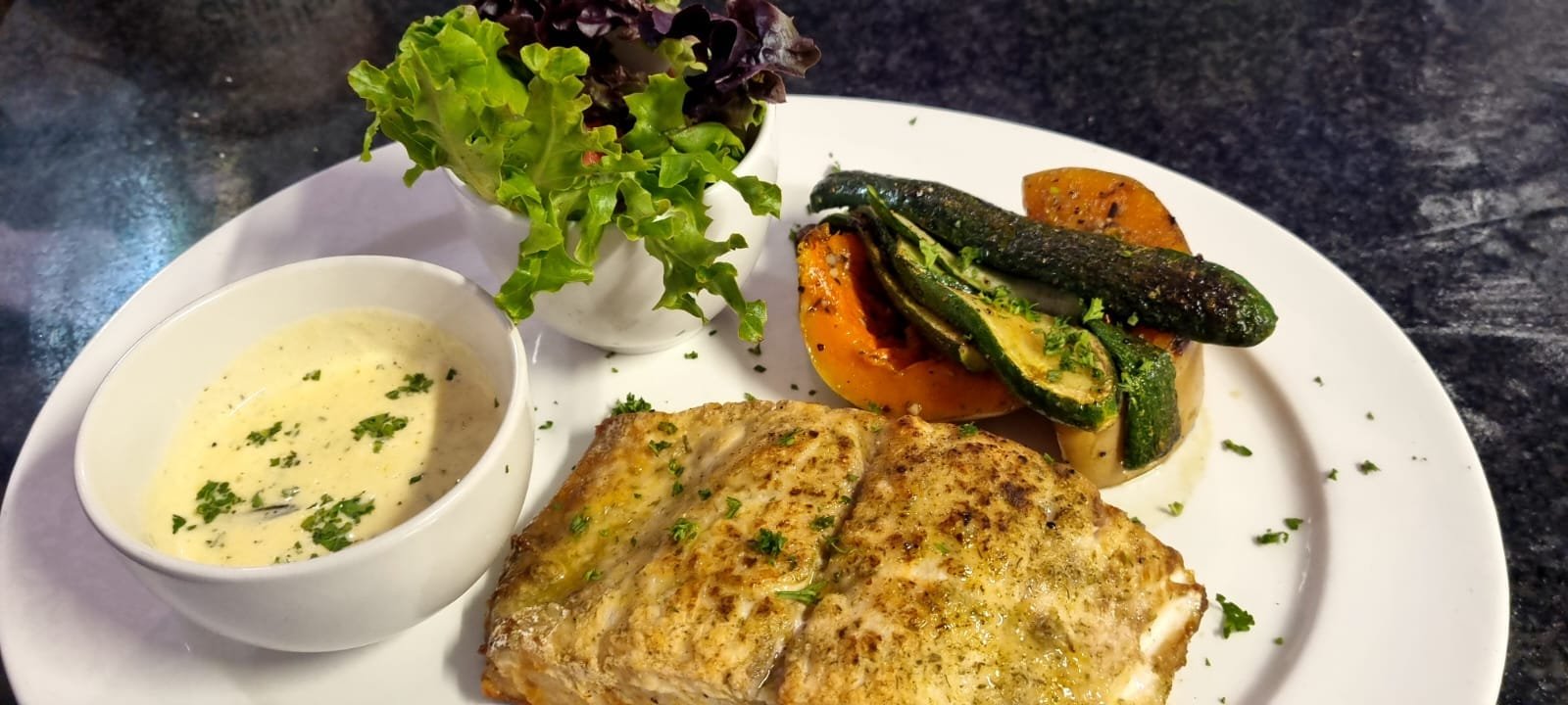 Grilled fish fillet with roasted vegetables, salad and a cream sauce