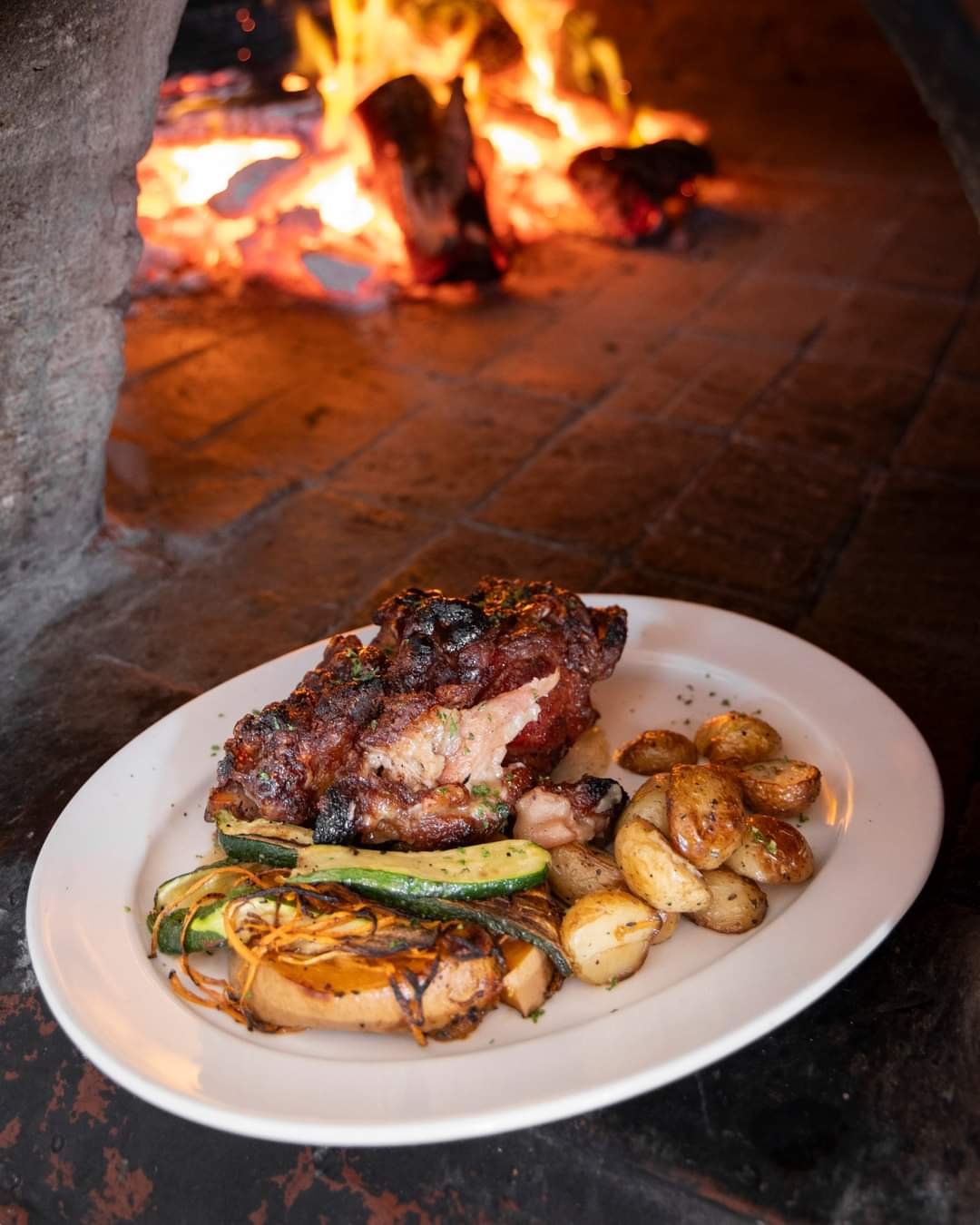 Pork ribs and grilled vegetables plated in front of the wood-fired oven